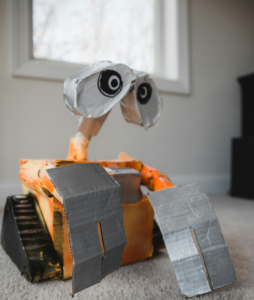 A robot made from cardboard on a carpet. We can see the window from this angle.